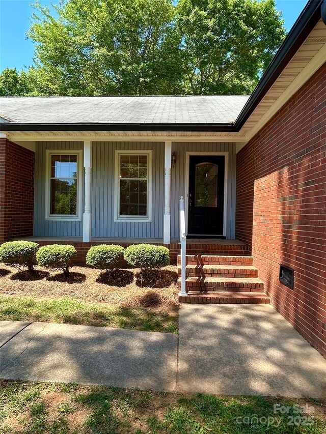 entrance to property featuring board and batten siding, a porch, brick siding, and roof with shingles