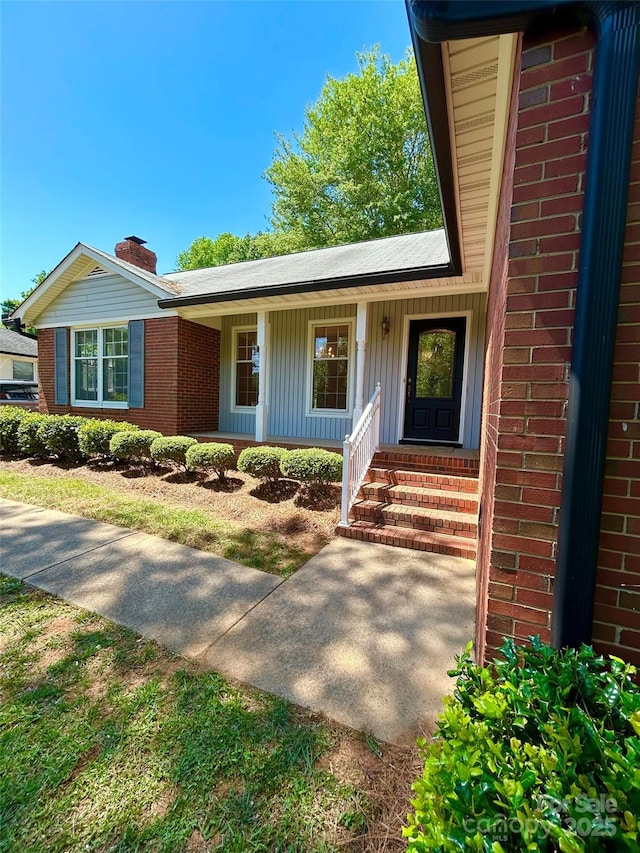view of front of house featuring brick siding, a chimney, and covered porch