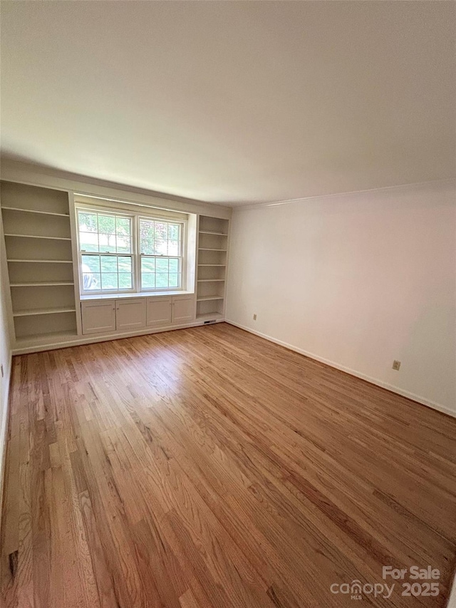 unfurnished room with wood finished floors, built in features, and baseboards
