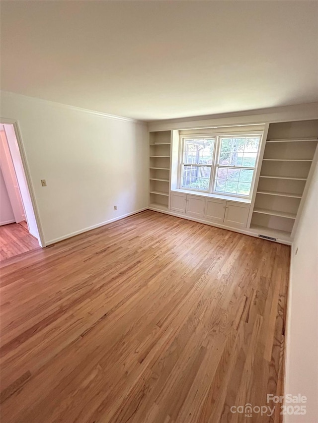 spare room with light wood-style floors, built in features, and baseboards