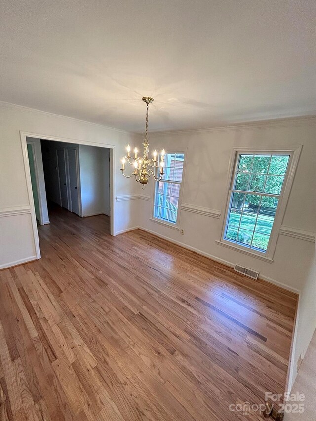 unfurnished dining area featuring a chandelier, light wood-style flooring, and ornamental molding