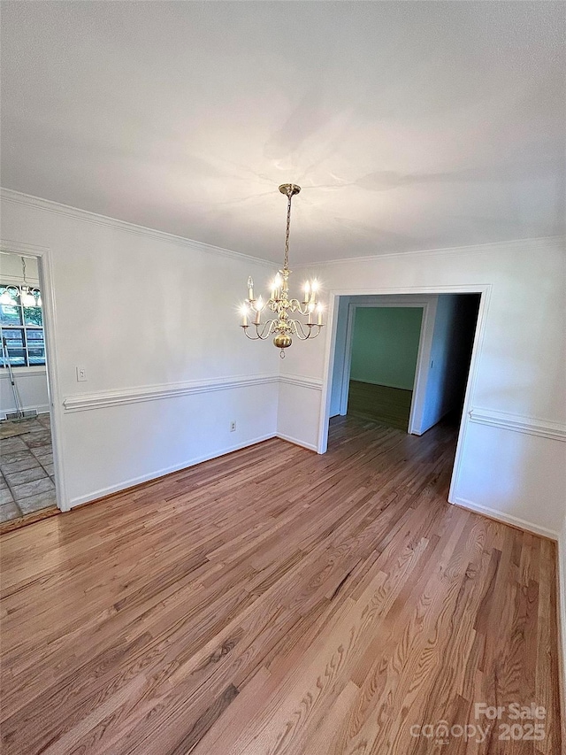 unfurnished dining area featuring a chandelier, wood finished floors, ornamental molding, and baseboards
