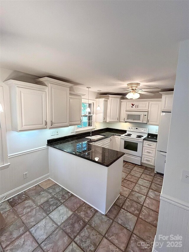 kitchen with white appliances, a peninsula, a sink, dark countertops, and white cabinets