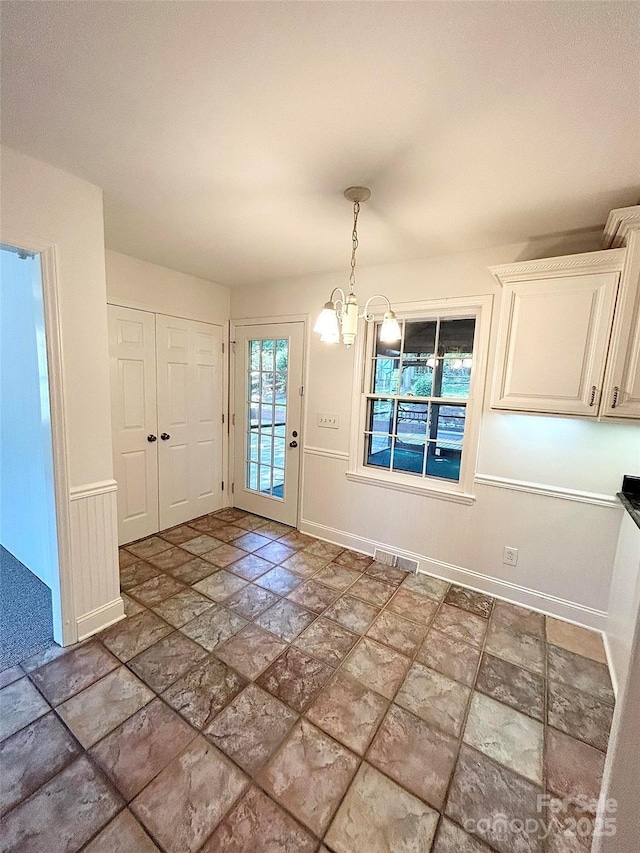 unfurnished dining area featuring stone tile floors, a chandelier, and baseboards
