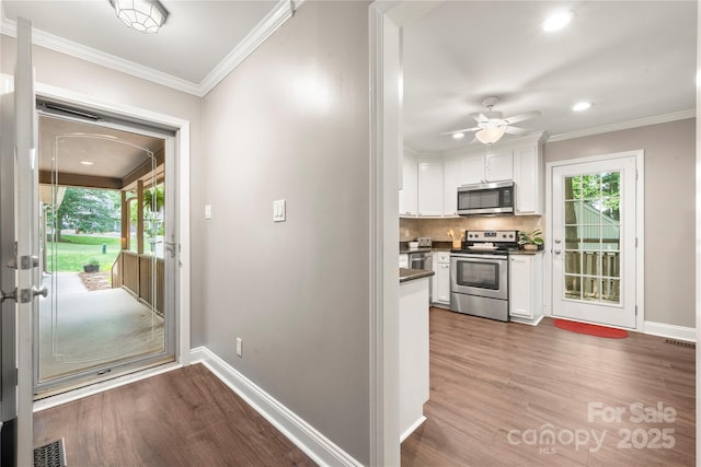 doorway featuring wood finished floors, healthy amount of natural light, baseboards, crown molding, and recessed lighting
