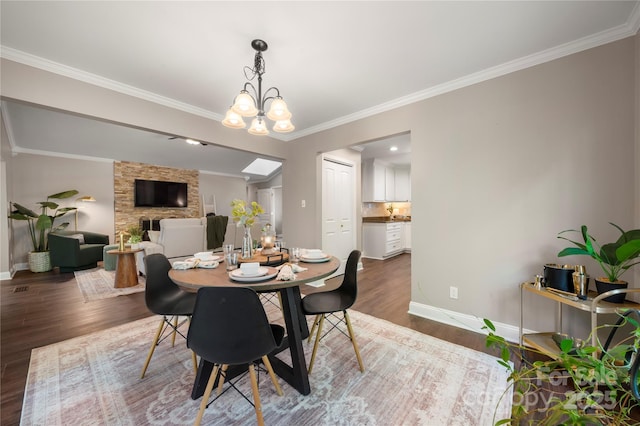 dining room with wood finished floors, baseboards, ornamental molding, a chandelier, and a fireplace