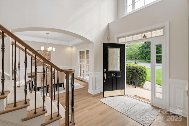 601 Carver Pond Ln, Waxhaw, NC 28173 - entrance foyer with arched walkways, light wood-style floors, a chandelier, ornamental molding, and a wainscoted wall
