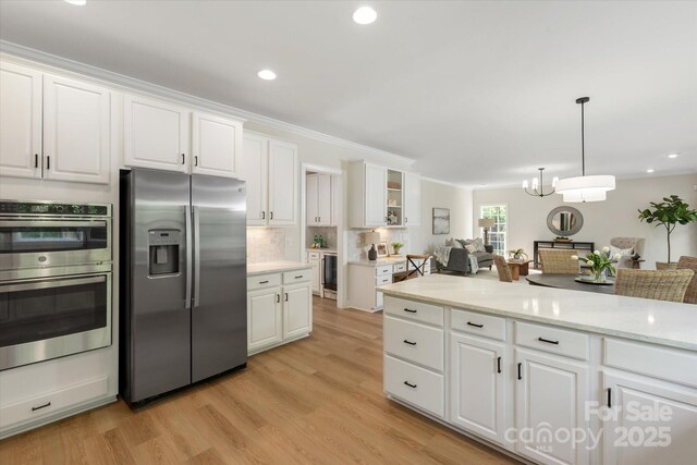 601 Carver Pond Ln, Waxhaw, NC 28173 - kitchen featuring appliances with stainless steel finishes, white cabinetry, light wood-style floors, decorative backsplash, and a chandelier