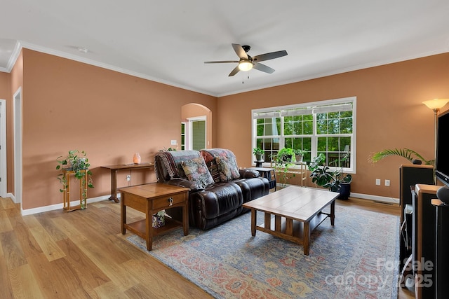 living room with ornamental molding, wood finished floors, ceiling fan, arched walkways, and baseboards