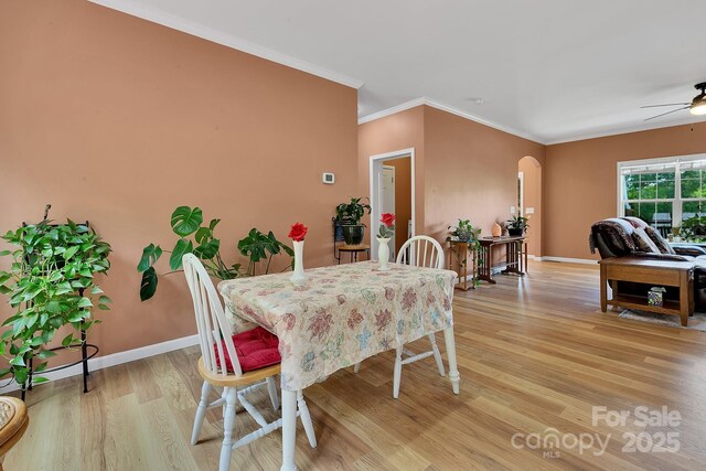 dining room featuring light wood-type flooring, crown molding, arched walkways, baseboards, and ceiling fan
