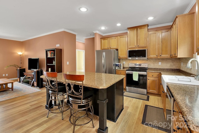 kitchen featuring stainless steel appliances, a center island, light wood-style floors, a breakfast bar, and crown molding