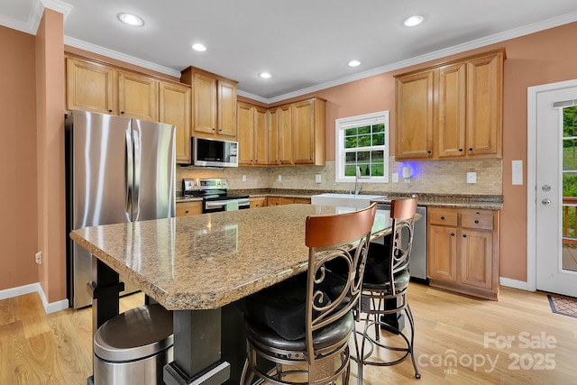 kitchen with appliances with stainless steel finishes, light wood finished floors, backsplash, a breakfast bar area, and ornamental molding