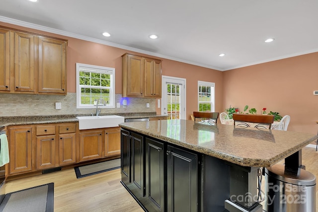 kitchen featuring a sink, light wood finished floors, tasteful backsplash, a kitchen breakfast bar, and crown molding