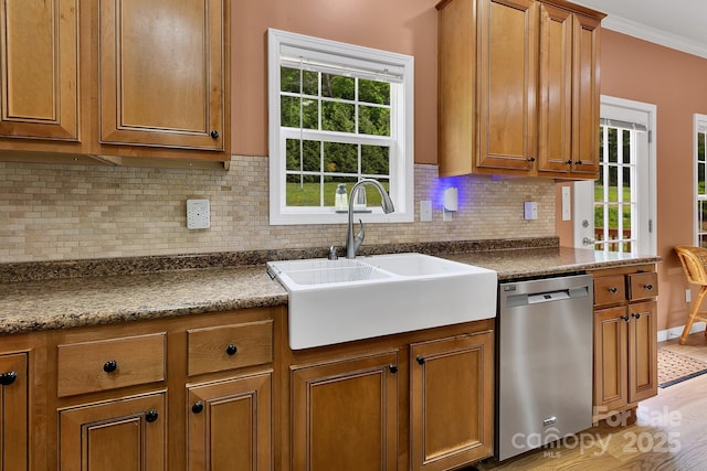 kitchen featuring dishwasher, a sink, brown cabinets, dark countertops, and crown molding