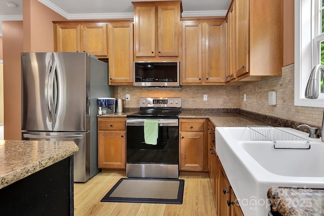 kitchen featuring stainless steel appliances, a sink, light wood finished floors, crown molding, and brown cabinets