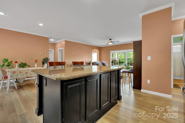 kitchen featuring dark cabinetry, ornamental molding, a ceiling fan, light wood finished floors, and baseboards