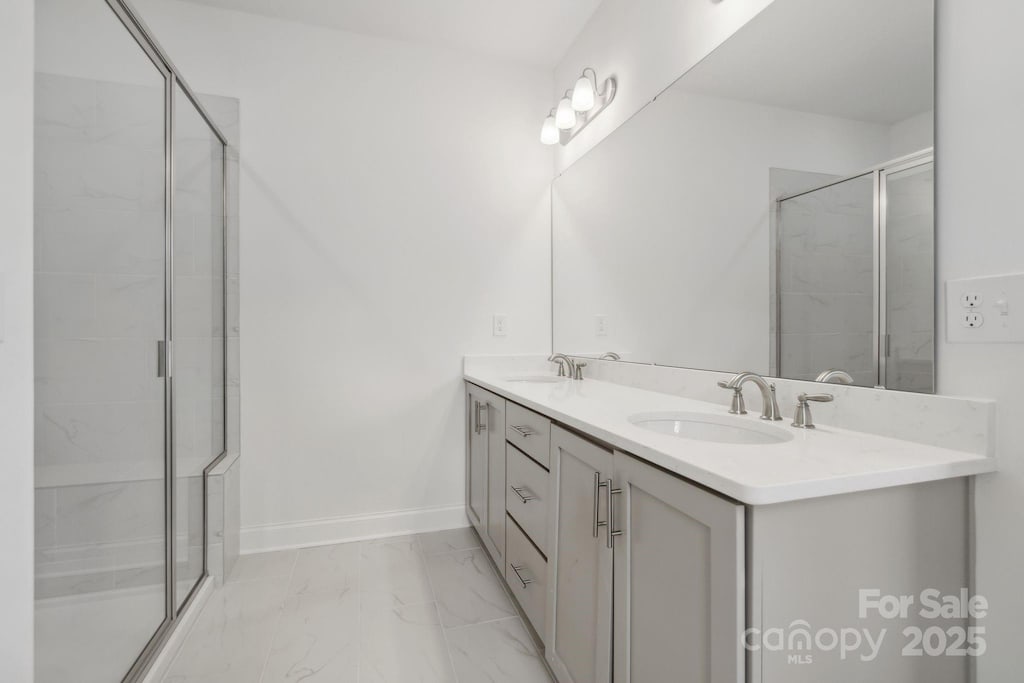 bathroom featuring marble finish floors, a shower stall, double vanity, and baseboards