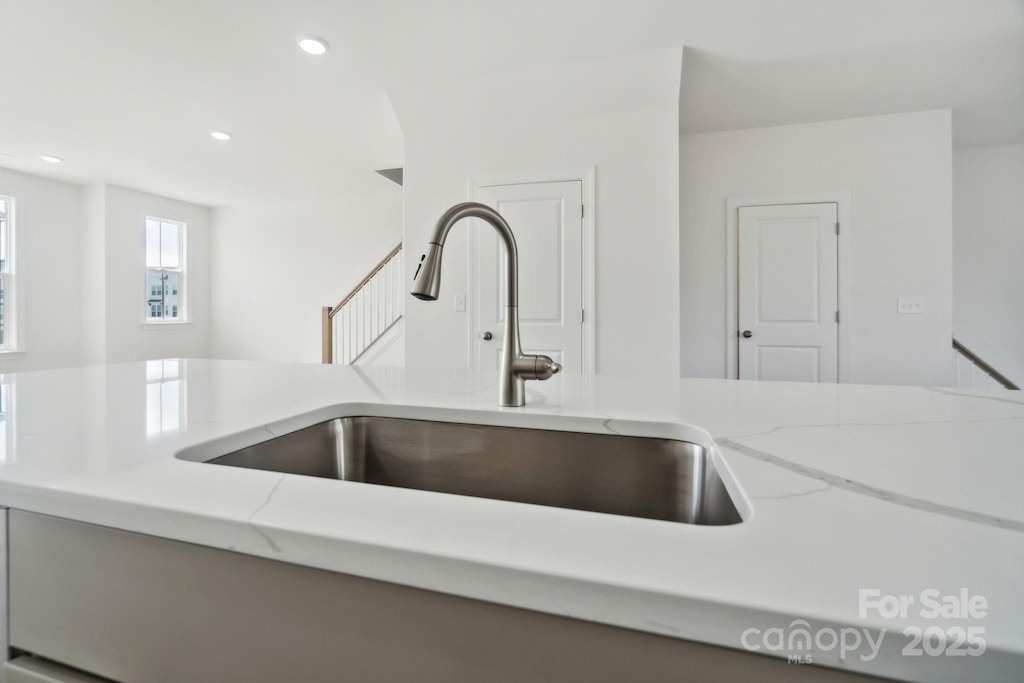 kitchen with a sink, light stone counters, and recessed lighting