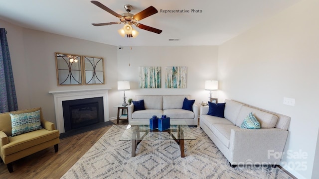 living room featuring wood finished floors, ceiling fan, a glass covered fireplace, and baseboards