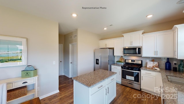 kitchen with stainless steel appliances, backsplash, dark wood-type flooring, a kitchen island, and light stone counters