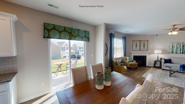 dining room with wood finished floors, a fireplace with flush hearth, baseboards, and ceiling fan
