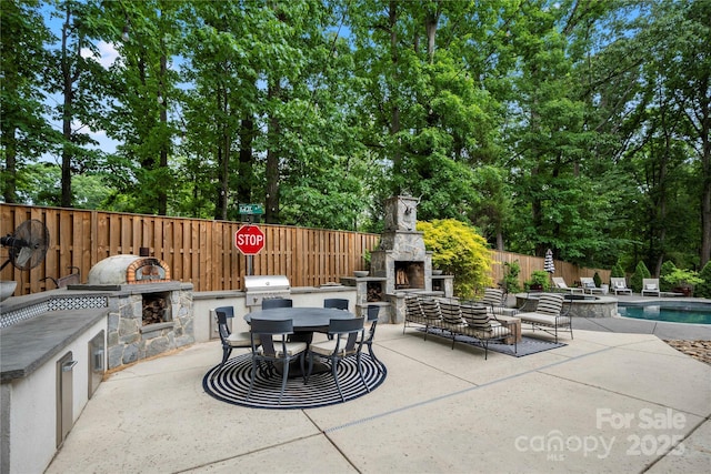 view of patio with an outdoor stone fireplace, an outdoor kitchen, fence, and area for grilling