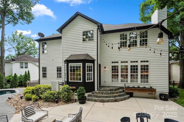 back of property with a patio, roof with shingles, an outdoor pool, and a chimney