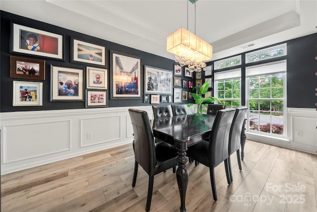 dining space with a chandelier, a decorative wall, crown molding, light wood-style flooring, and wainscoting