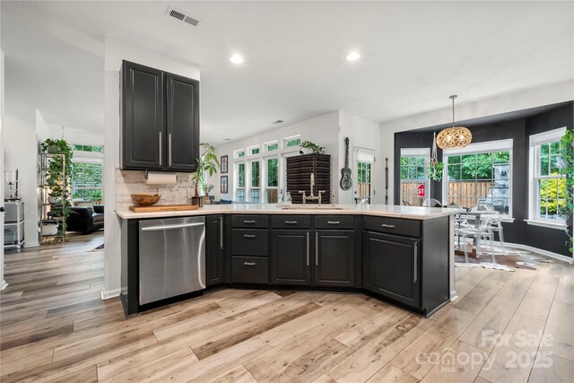 kitchen featuring dishwasher, a sink, a peninsula, light countertops, and light wood-style floors