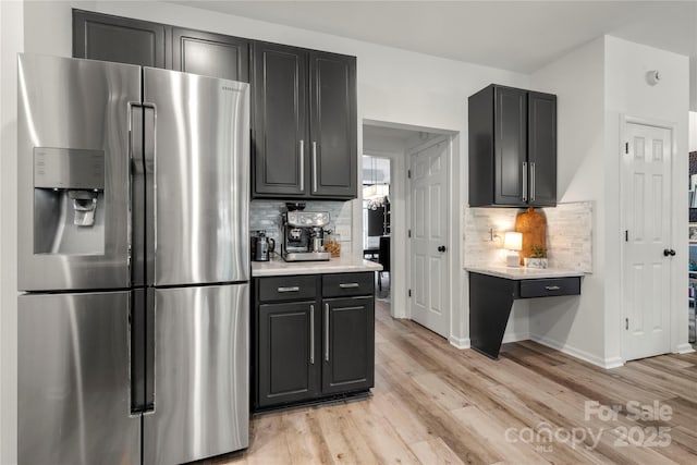 kitchen with stainless steel fridge with ice dispenser, light wood finished floors, decorative backsplash, and light countertops