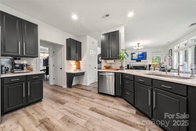 kitchen with a sink, stainless steel dishwasher, a chandelier, light countertops, and decorative backsplash