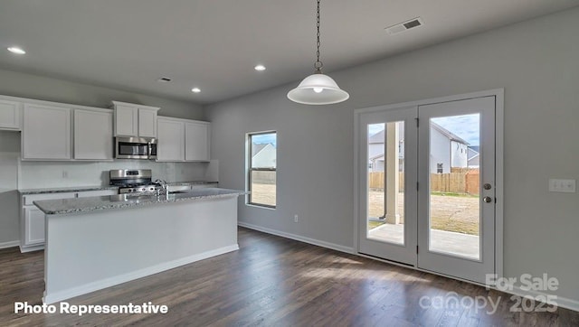 kitchen with stainless steel appliances, dark wood-type flooring, white cabinets, baseboards, and a kitchen island with sink