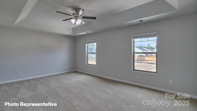 spare room with a raised ceiling, carpet, ceiling fan, and baseboards
