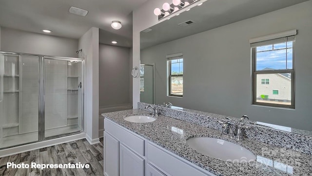 bathroom with a stall shower, wood finished floors, double vanity, and recessed lighting