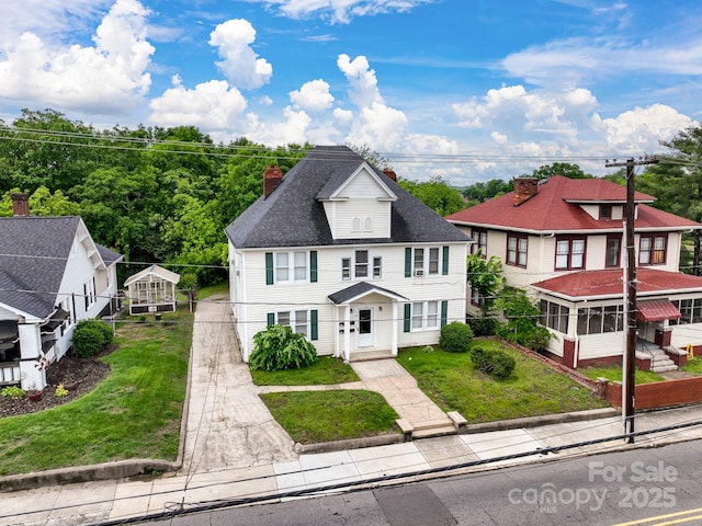 view of front of home with a chimney, concrete driveway, a front lawn, a shingled roof, and a sunroom