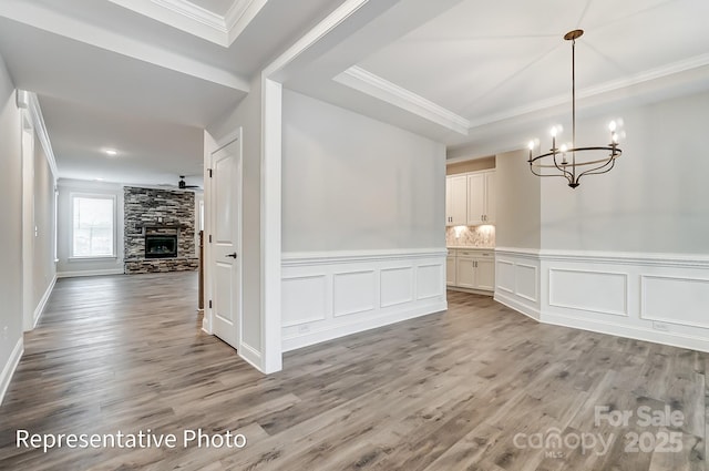 unfurnished dining area featuring crown molding, a chandelier, wood finished floors, a decorative wall, and a fireplace
