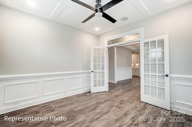 empty room with french doors, coffered ceiling, a decorative wall, ceiling fan, and wood finished floors