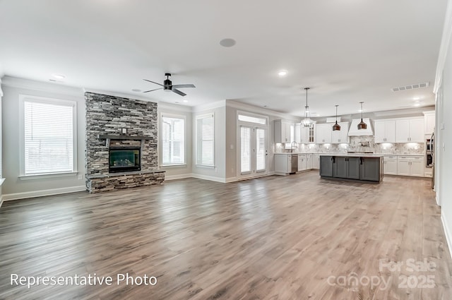 unfurnished living room featuring crown molding, ceiling fan, a fireplace, light wood finished floors, and baseboards