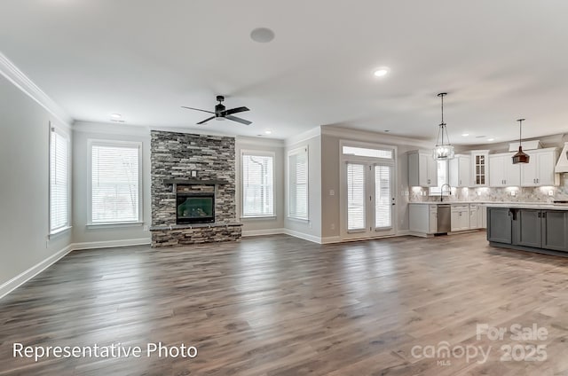 unfurnished living room featuring crown molding, ceiling fan, a stone fireplace, baseboards, and dark wood-type flooring