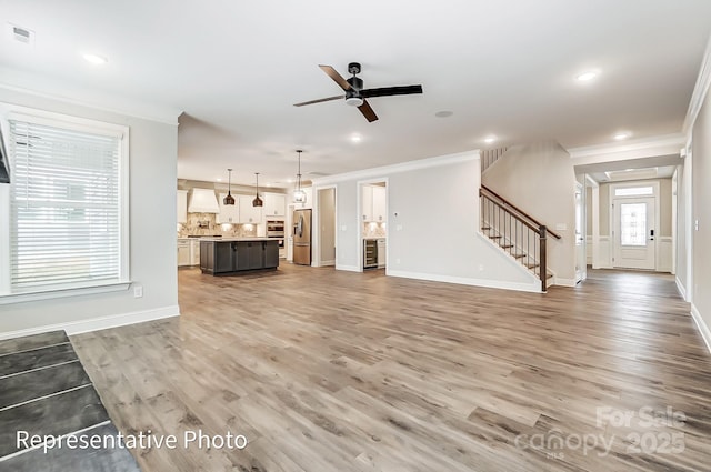 unfurnished living room featuring ornamental molding, stairs, light wood finished floors, baseboards, and a ceiling fan