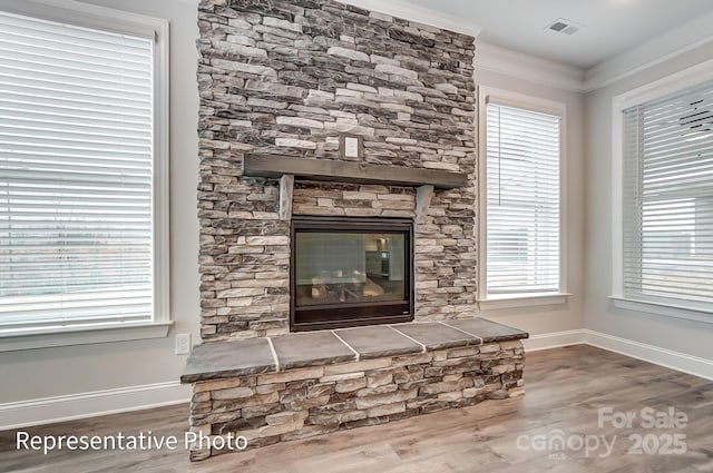 detailed view of wood finished floors, baseboards, a fireplace, and crown molding