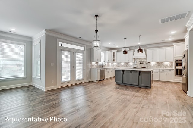 kitchen with gray cabinetry, premium range hood, stainless steel appliances, backsplash, and crown molding
