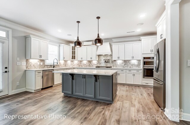 kitchen with stainless steel appliances, custom range hood, gray cabinets, white cabinetry, and light countertops