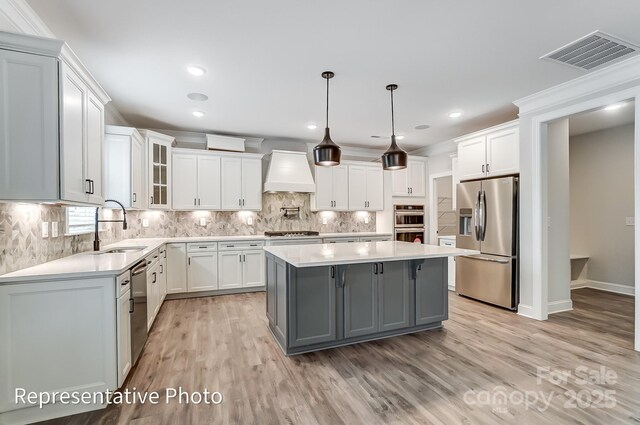 kitchen with appliances with stainless steel finishes, a sink, gray cabinetry, premium range hood, and light wood-style floors