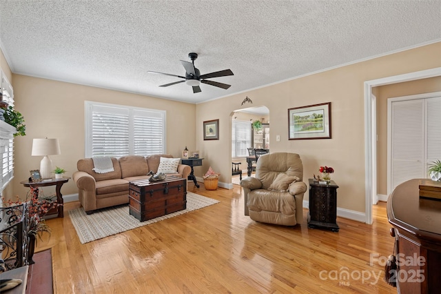 living room featuring arched walkways, ceiling fan, light wood-style floors, a textured ceiling, and baseboards