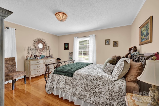 bedroom with a textured ceiling, crown molding, and light wood-style flooring