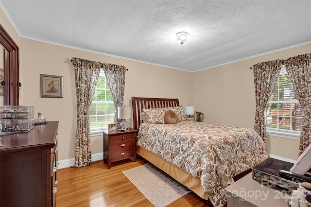 bedroom with light wood-style flooring, a textured ceiling, crown molding, and baseboards