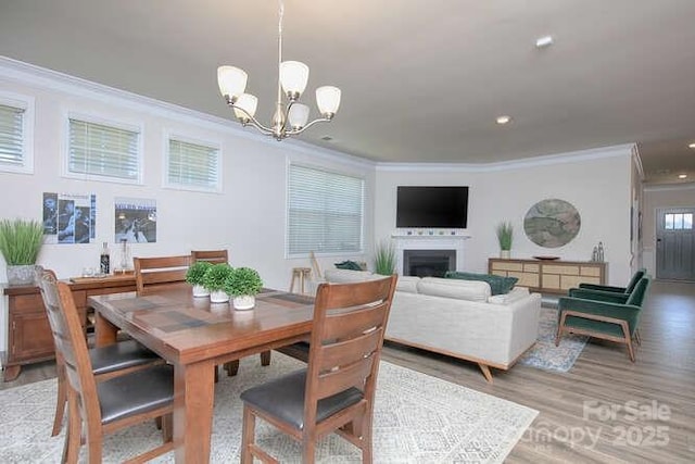 dining area featuring crown molding, light wood-style flooring, a chandelier, a fireplace, and recessed lighting