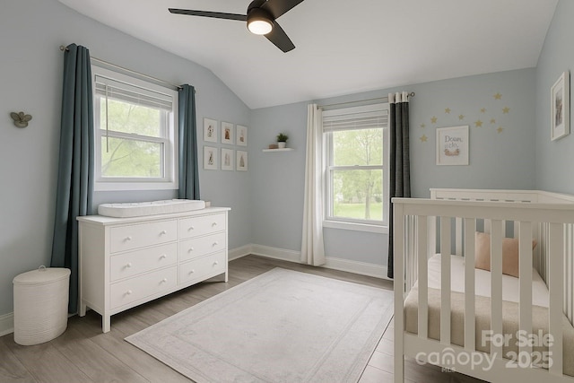 bedroom featuring multiple windows, lofted ceiling, light wood-style flooring, a crib, and baseboards