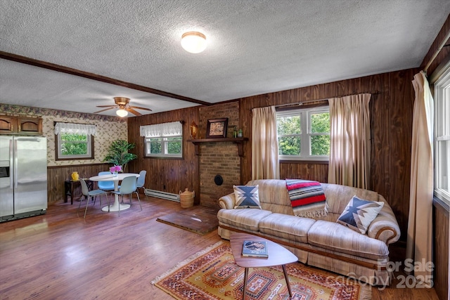 living area featuring a baseboard heating unit, a textured ceiling, wood finished floors, wood walls, and ceiling fan